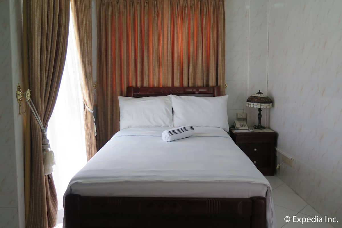 Une chambre d’hôtel avec un lit, des rideaux, une table de chevet avec une lampe et un téléphone.