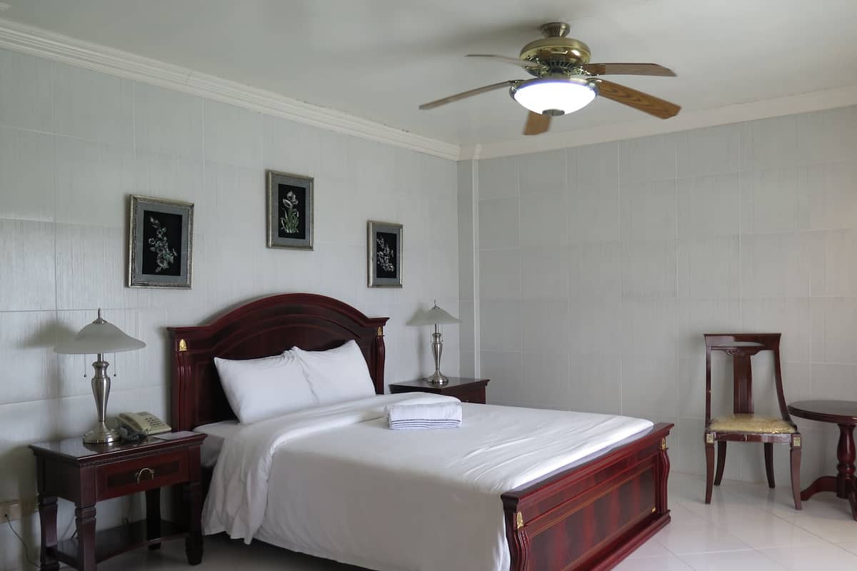 Une chambre d’hôtel avec un grand lit, deux tables de chevet, un ventilateur de plafond et des œuvres d’art encadrées accrochées au mur.