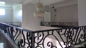 Un interior espacioso con un alto techo, una lámpara decorativa de araña y una barandilla de hierro forjado negro.
