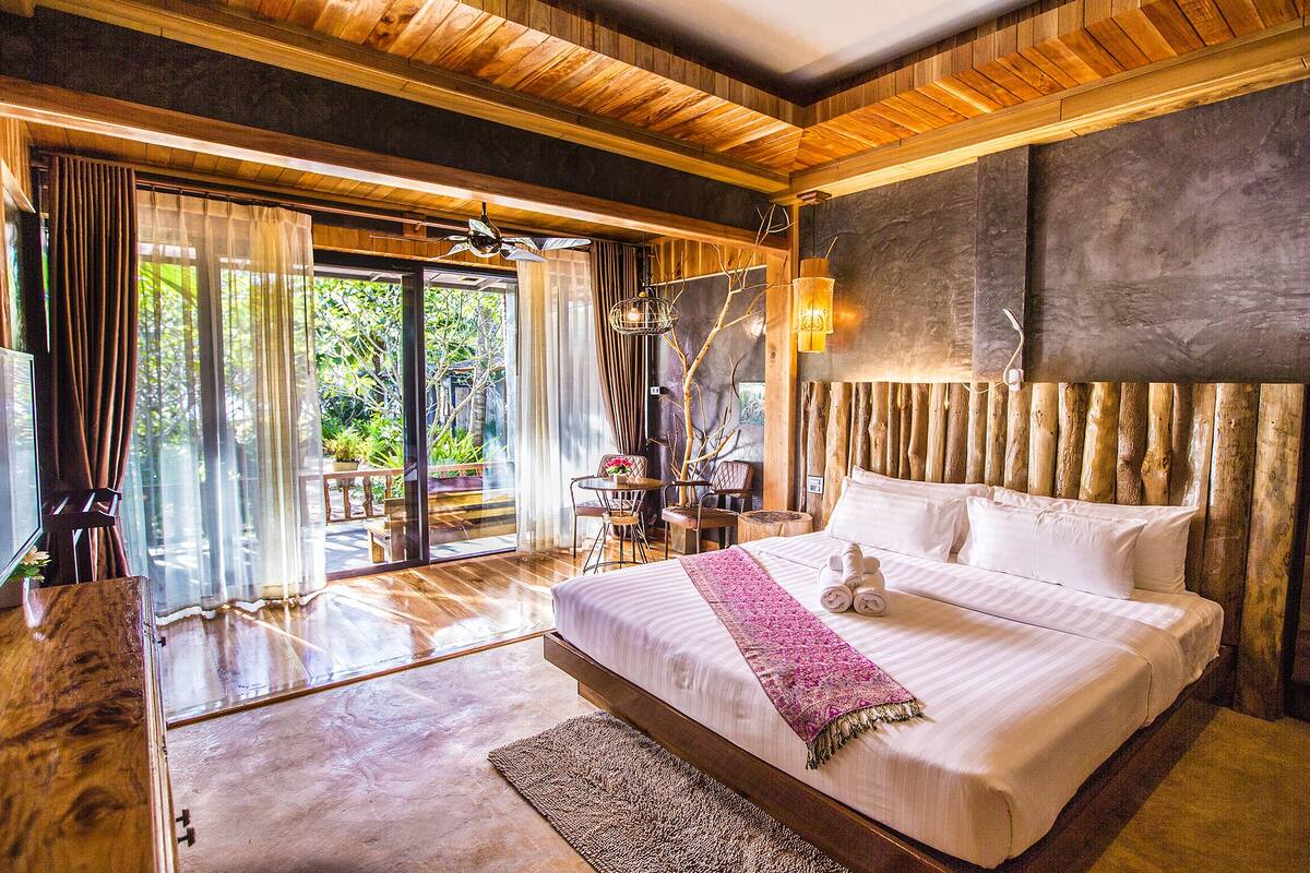 A spacious bedroom with a large bed, wooden ceiling, and a view of the outdoors.