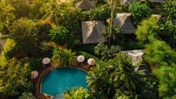 An aerial view of a resort with a swimming pool surrounded by palm trees and thatched-roof huts, overlooking a beach. - Andalay Beach Resort Koh Libong (Ko Libong)