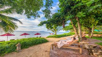 A beachside lounge area with wooden loungers, red umbrellas, and a view of the sea.