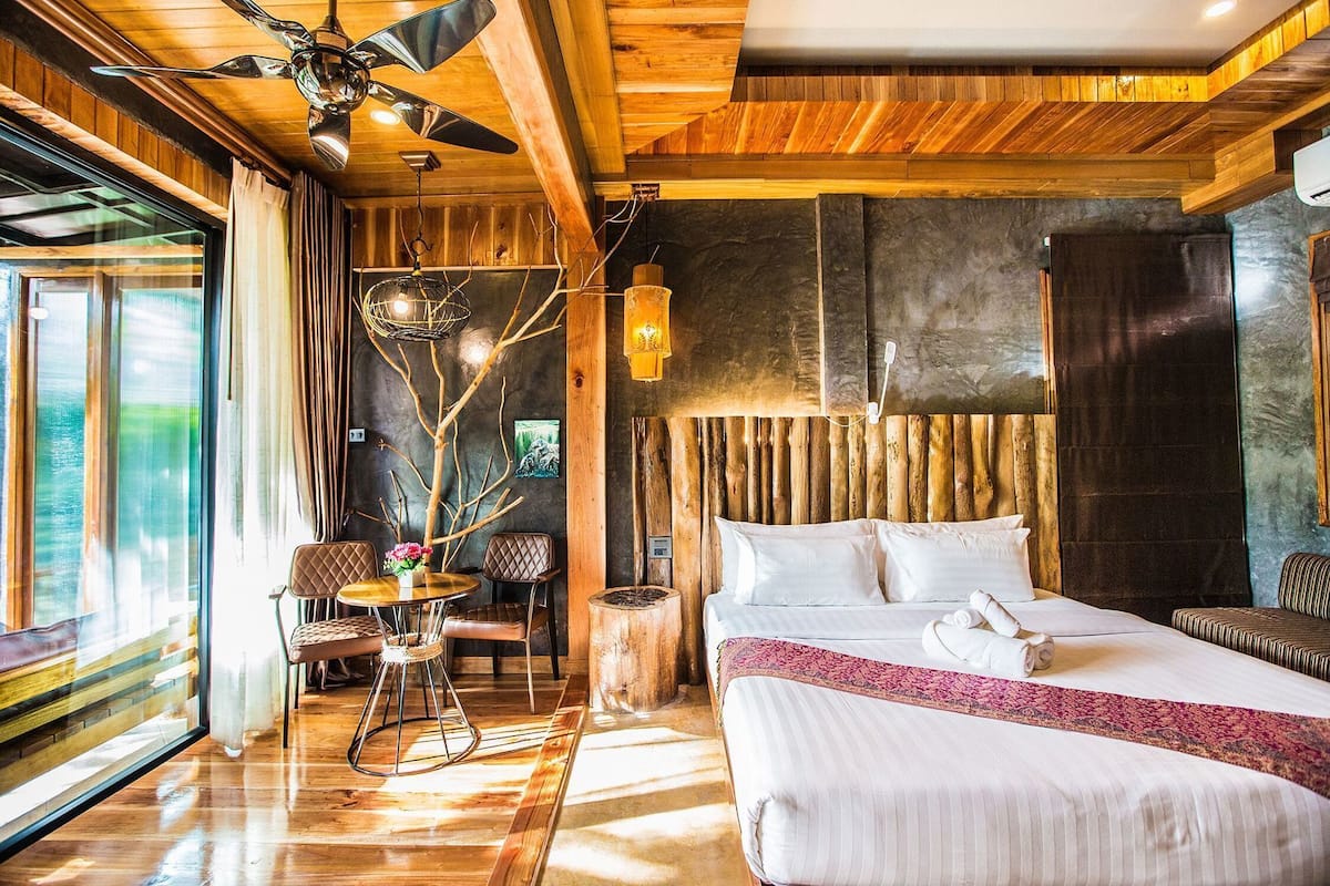 A hotel room with a bed, a seating area with chairs, a dining table, and a large window.