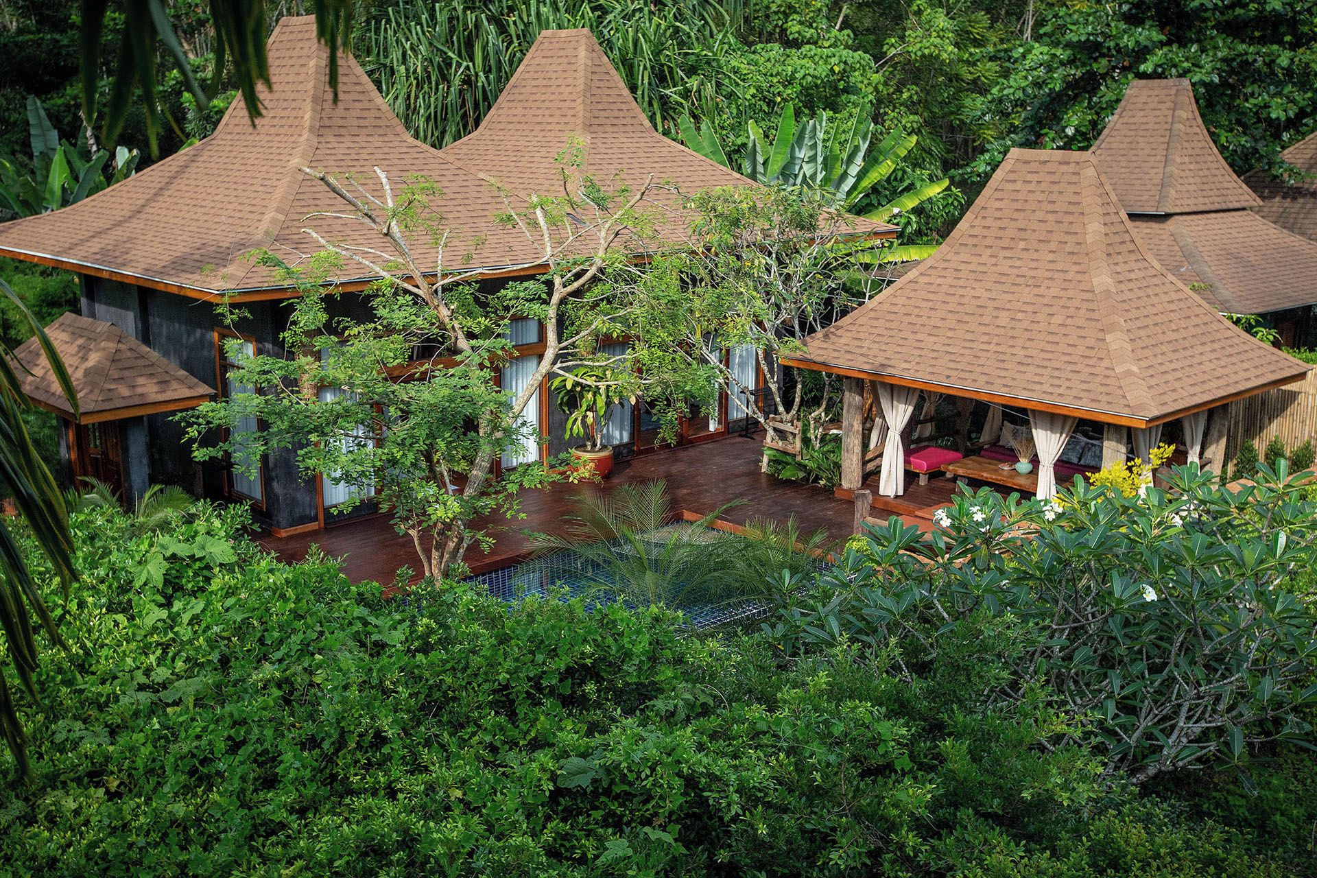 Un resort tropical con varias construcciones tipo bungalow, cada una con techo a dos aguas, rodeadas de exuberante vegetación.