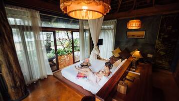 A bedroom with a large bed, a wooden floor, a hanging lamp, and a view of the outdoors.