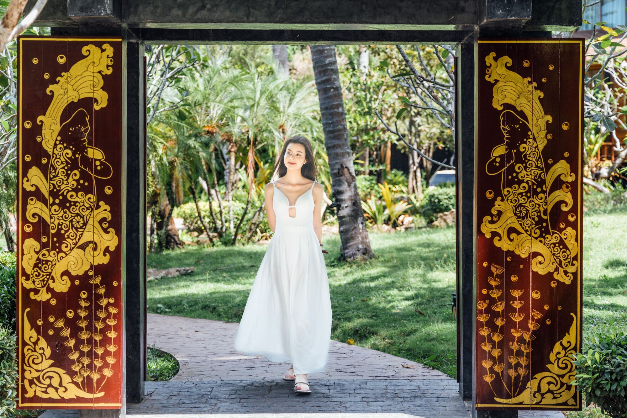 A woman in a white dress standing under a decorative archway with intricate golden designs.