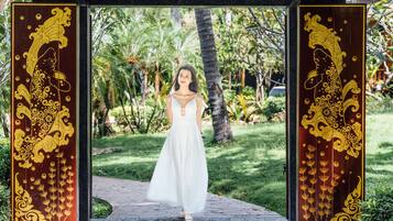 A woman in a white dress standing under a decorative archway with intricate golden designs.