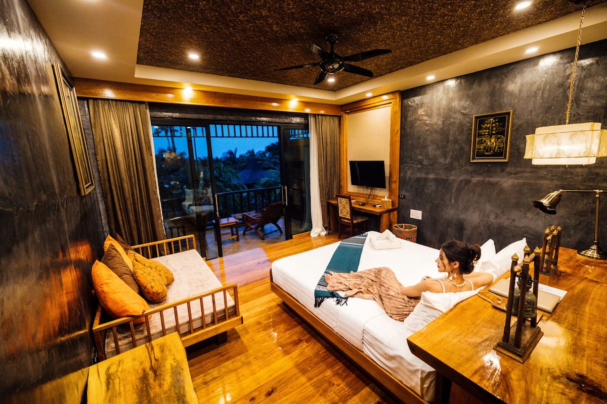 A hotel room with a bed, a desk, a chair, a TV, and a balcony with curtains.