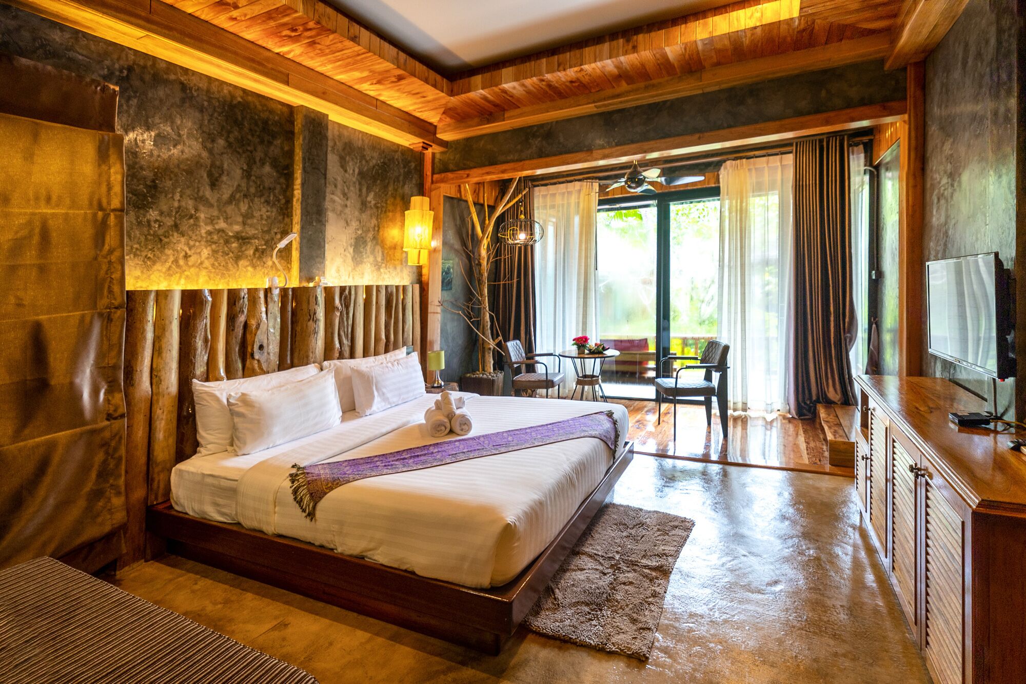 A wooden-floored bedroom with a large bed, a desk, and a television.