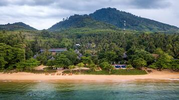 A tropical beach resort with a mountain backdrop, clear waters, and lush greenery.