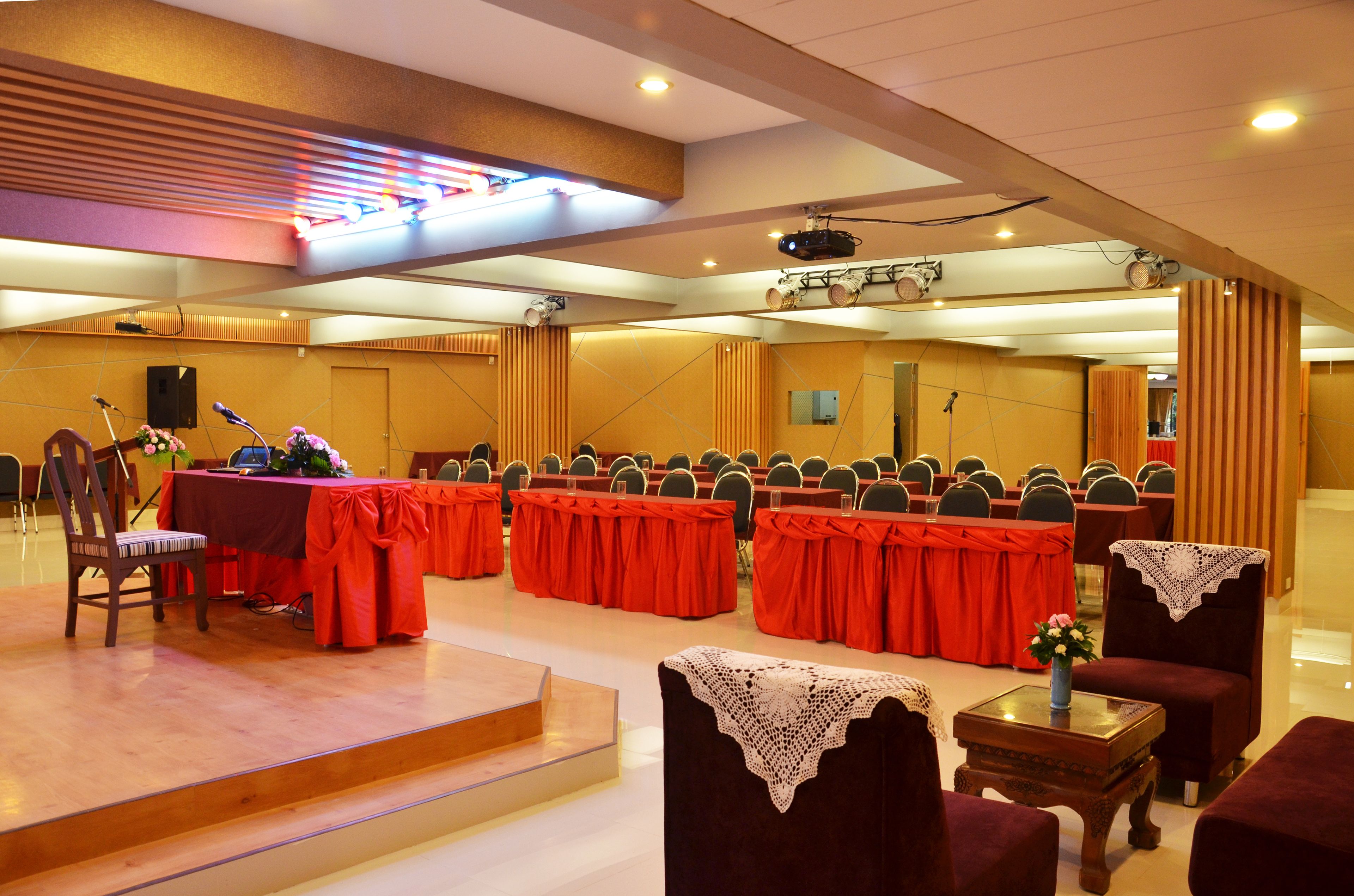 A conference room with rows of tables and chairs, a stage with a podium, and a projector.