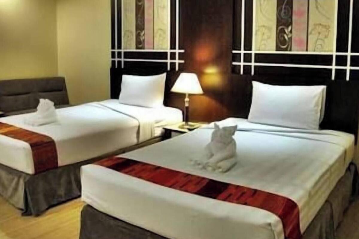 Two twin beds with white linens and a red and brown striped blanket, a nightstand with a lamp, and a wall with a decorative panel.