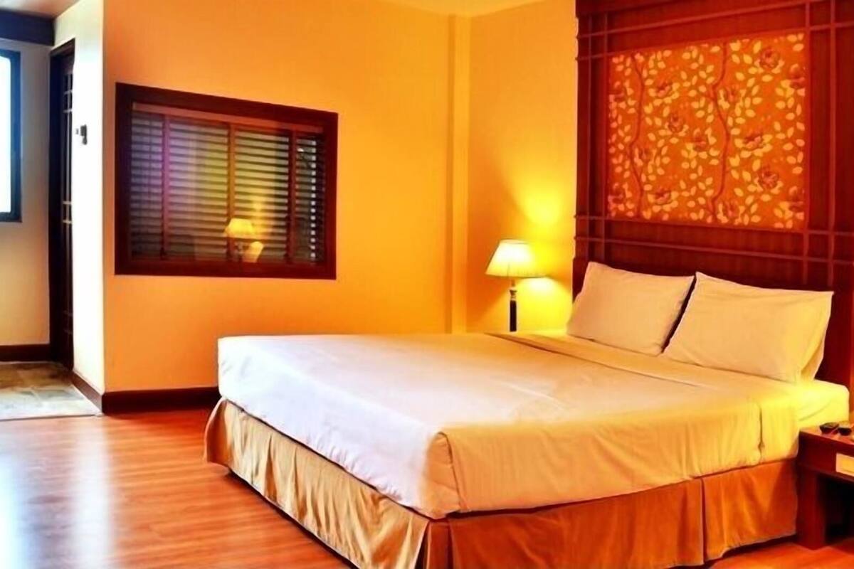 A hotel room with a bed, two bedside lamps, a wooden headboard, and a window with blinds.