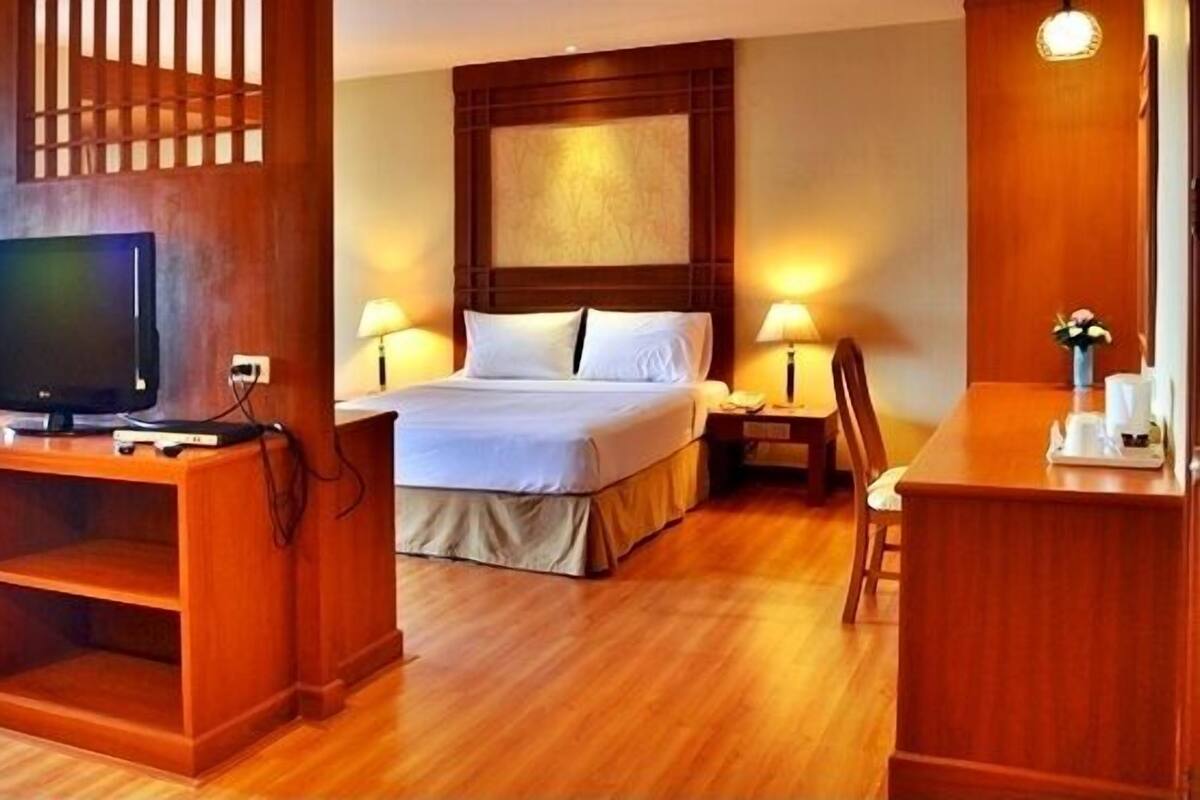 A hotel room with a bed, bedside tables, a TV, and a wooden entertainment unit.