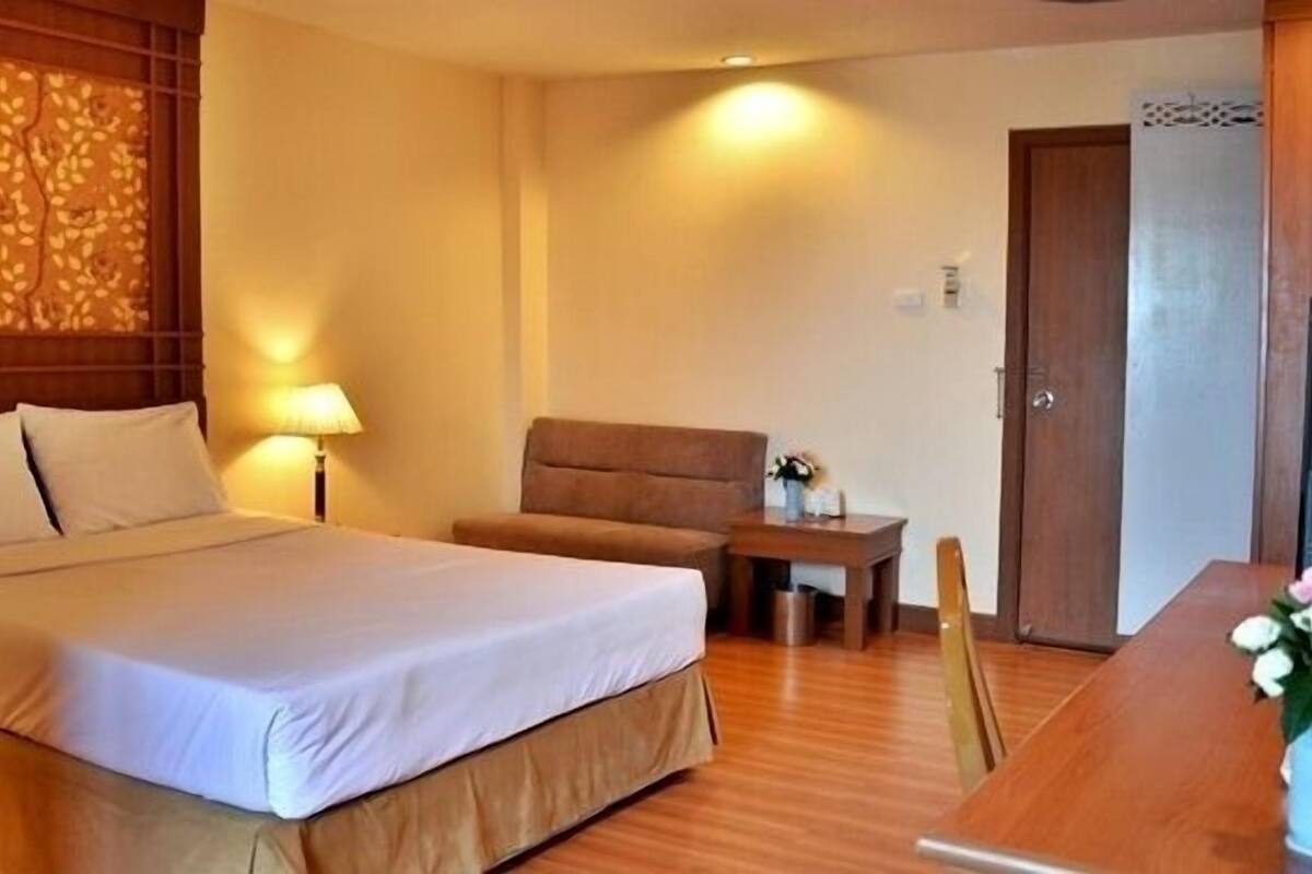 A hotel room with a large bed, a wooden headboard, a small table with a lamp, a chair, and a wooden desk.