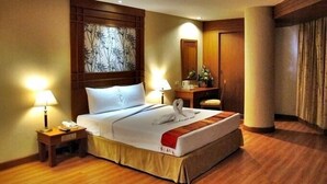 A hotel room with a neatly made bed, a bedside table with a lamp, a wooden headboard, a mirror, and a wooden floor. - Friendlytel Hotel (Hat Yai)