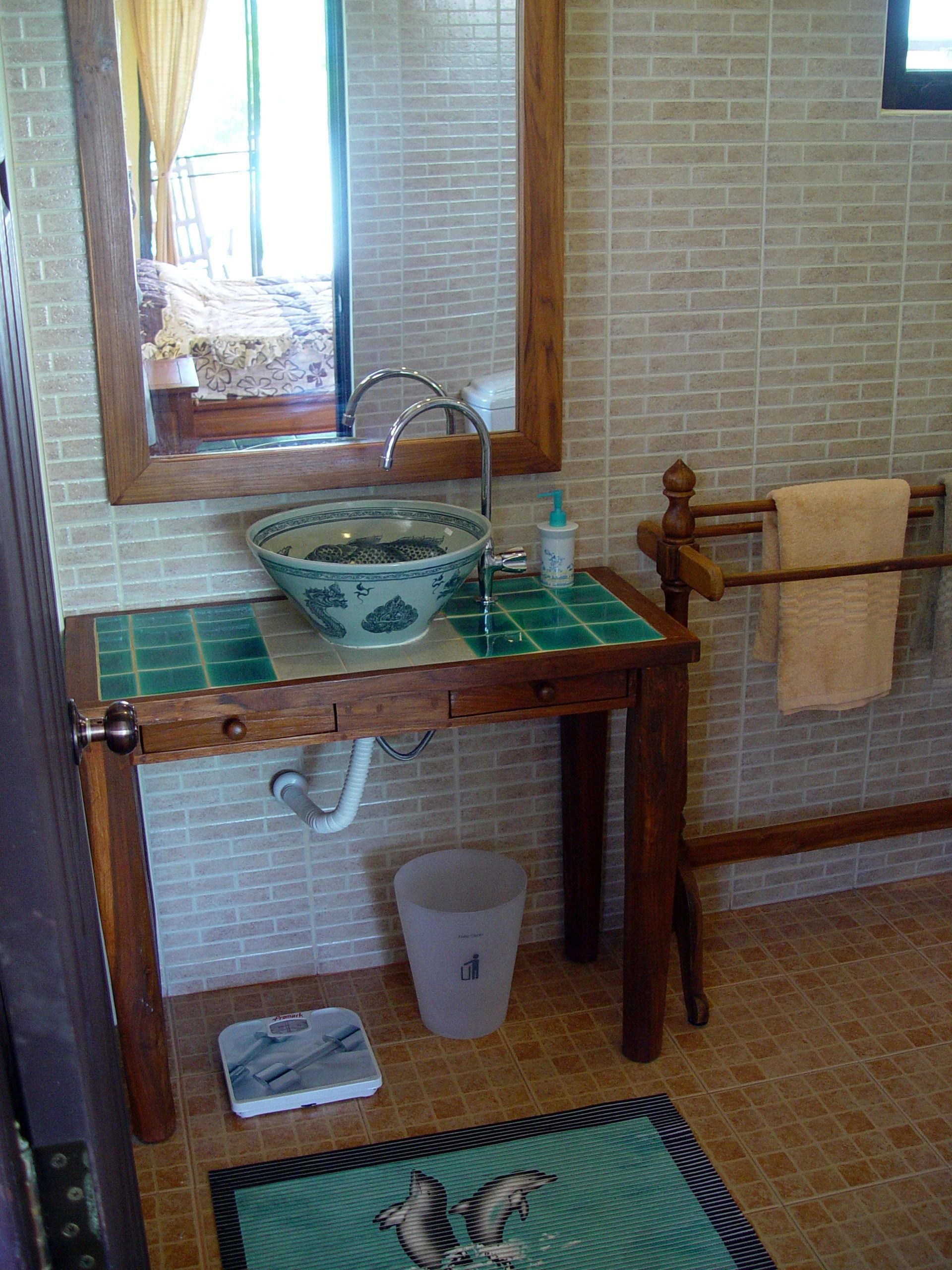 A bathroom with a wooden sink, a mirror, a towel rack, and a trash bin.