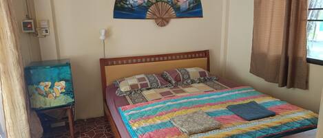 A bedroom with a bed, a wall-mounted fan, a small table, and a decorative wall piece.
