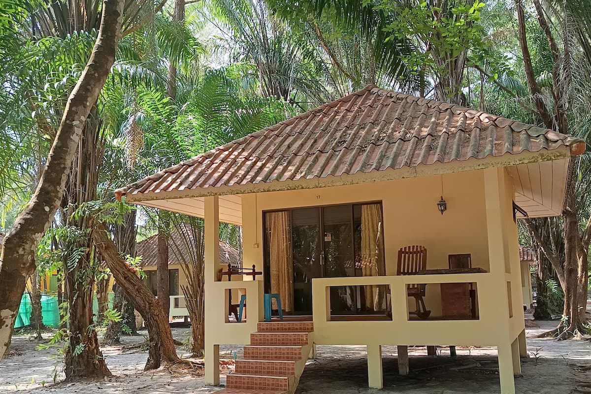 A small, single-story structure with a tiled roof, surrounded by trees, and featuring a staircase leading to an entrance.