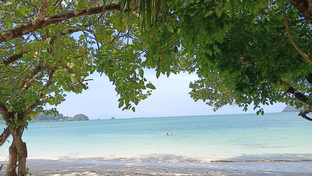A beach with two wooden chairs under a tree, a clear view of the ocean, and distant islands. - Buffalo Bay Vacation Club (Ranong)