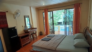 A bedroom with a bed, a desk, a mirror, a fan, and a view of the outdoors. - Buffalo Bay Vacation Club (Ranong)