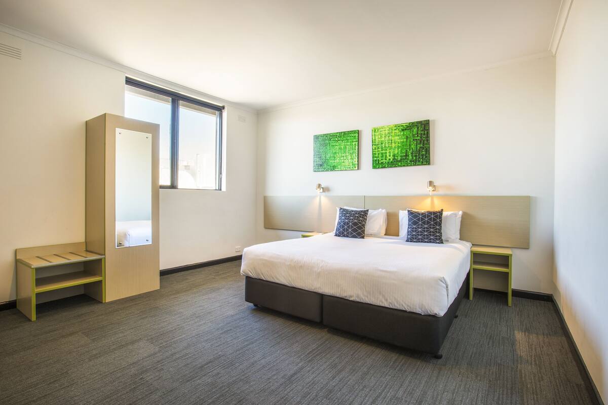 A hotel room with a large bed, a bedside table, a nightstand, a built-in bench, and a window.