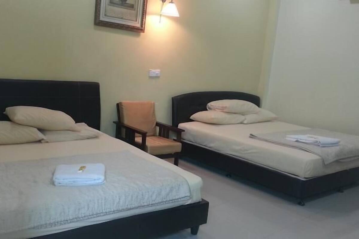 Habitación de hotel con dos camas, una silla y una lámpara fijada a la pared.