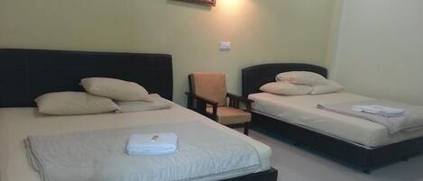 A hotel room with two beds, a chair, and a wall-mounted lamp.