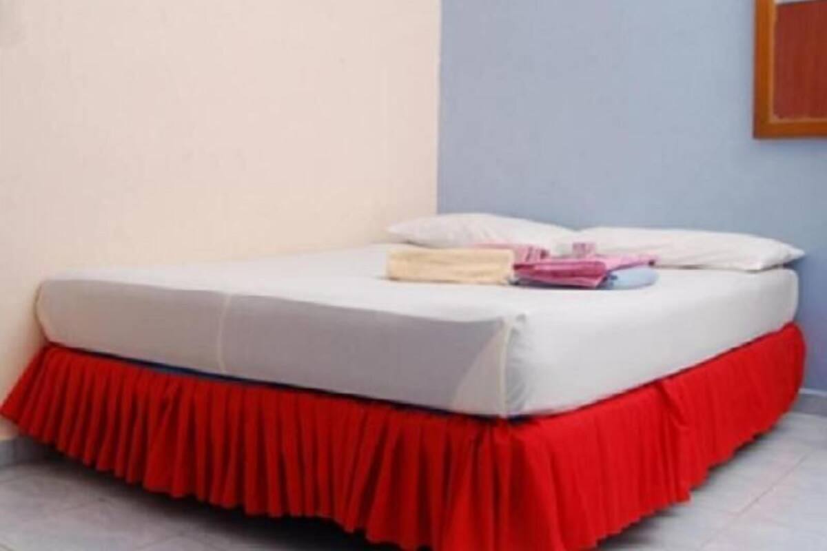 Una cama con falda roja, almohadas blancas y toallas dobladas sobre un colchón blanco.