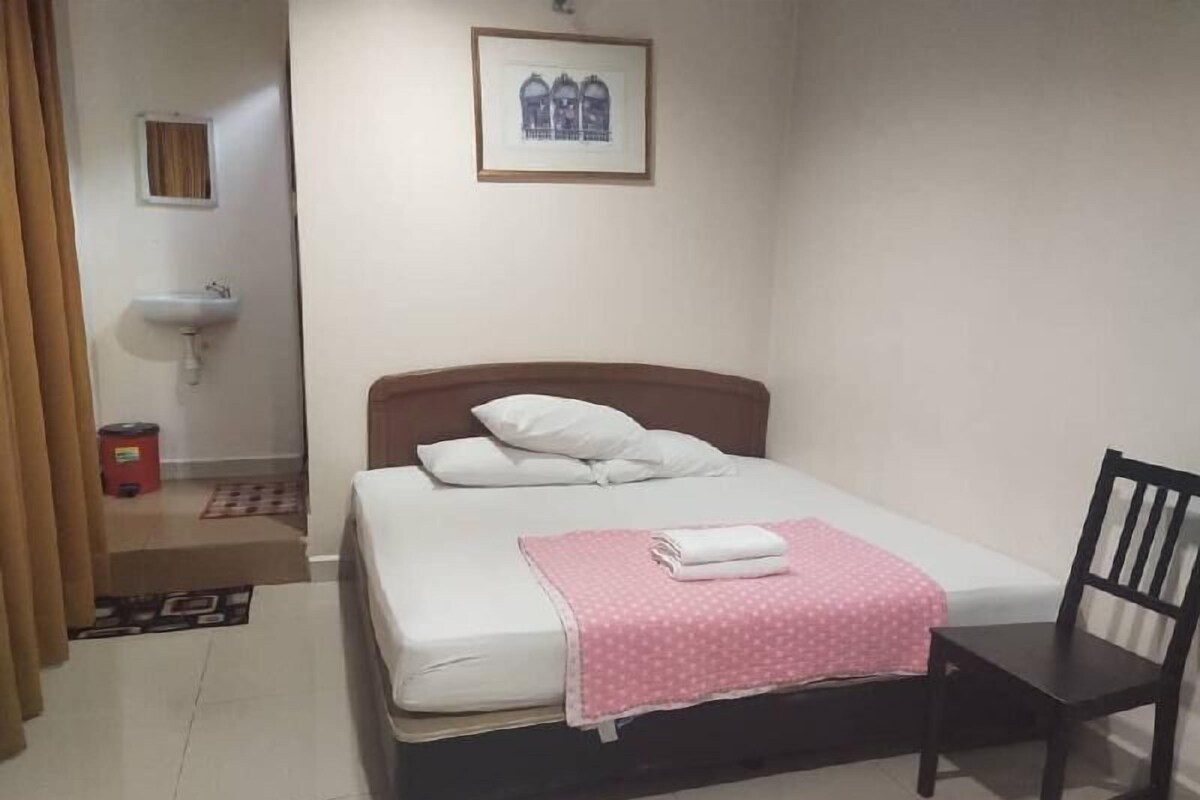 Un dormitorio con cama, una silla, un lavamanos y un cuadro en la pared.