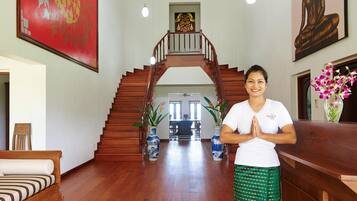 A person standing in a room with a wooden staircase, a large red painting, and a Buddha statue.