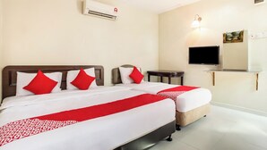 Ein Hotelzimmer mit zwei Betten, jeweils mit roter und weißer Bettwäsche, einem an der Wand befestigten Flachbildfernseher und einem kleinen Tisch neben den Betten.