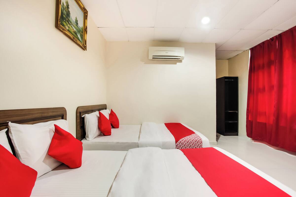 Een hotelkamer met twee bedden, rood-wit beddengoed, een schilderij aan de muur, een airconditioning en een rood gordijn.