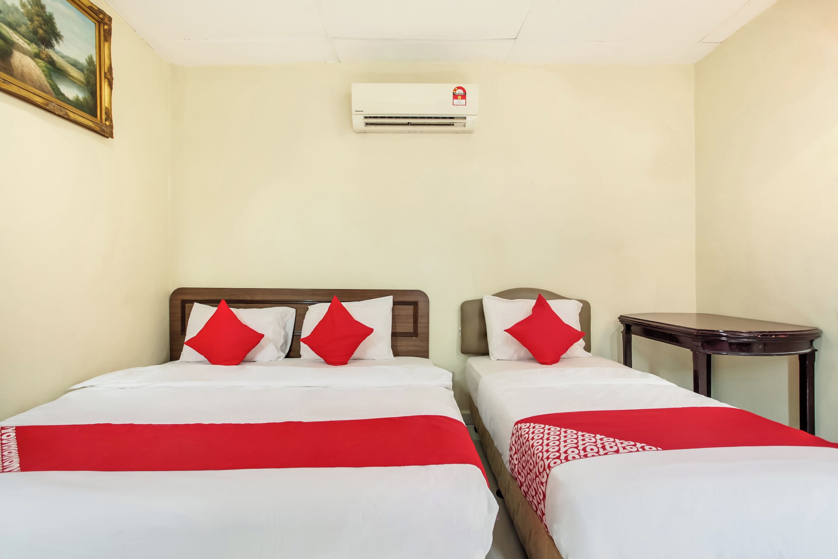 Una habitación de hotel con dos camas, cada una con ropa de cama roja y blanca, y una pequeña mesa.