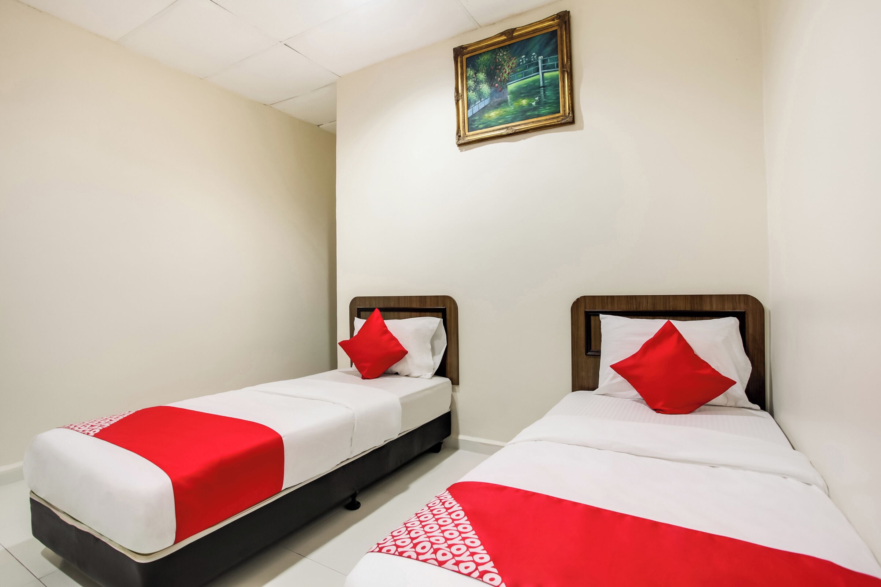 Habitación de hotel con dos camas individuales, cada una con una colcha roja y blanca y almohadas a juego.
