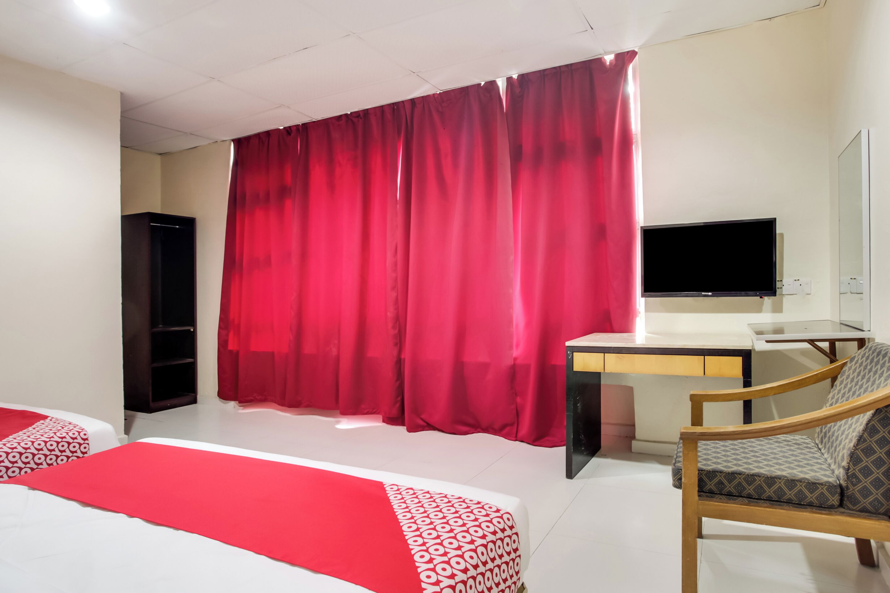 Una habitación de hotel con cama, escritorio, silla, televisor y armario.