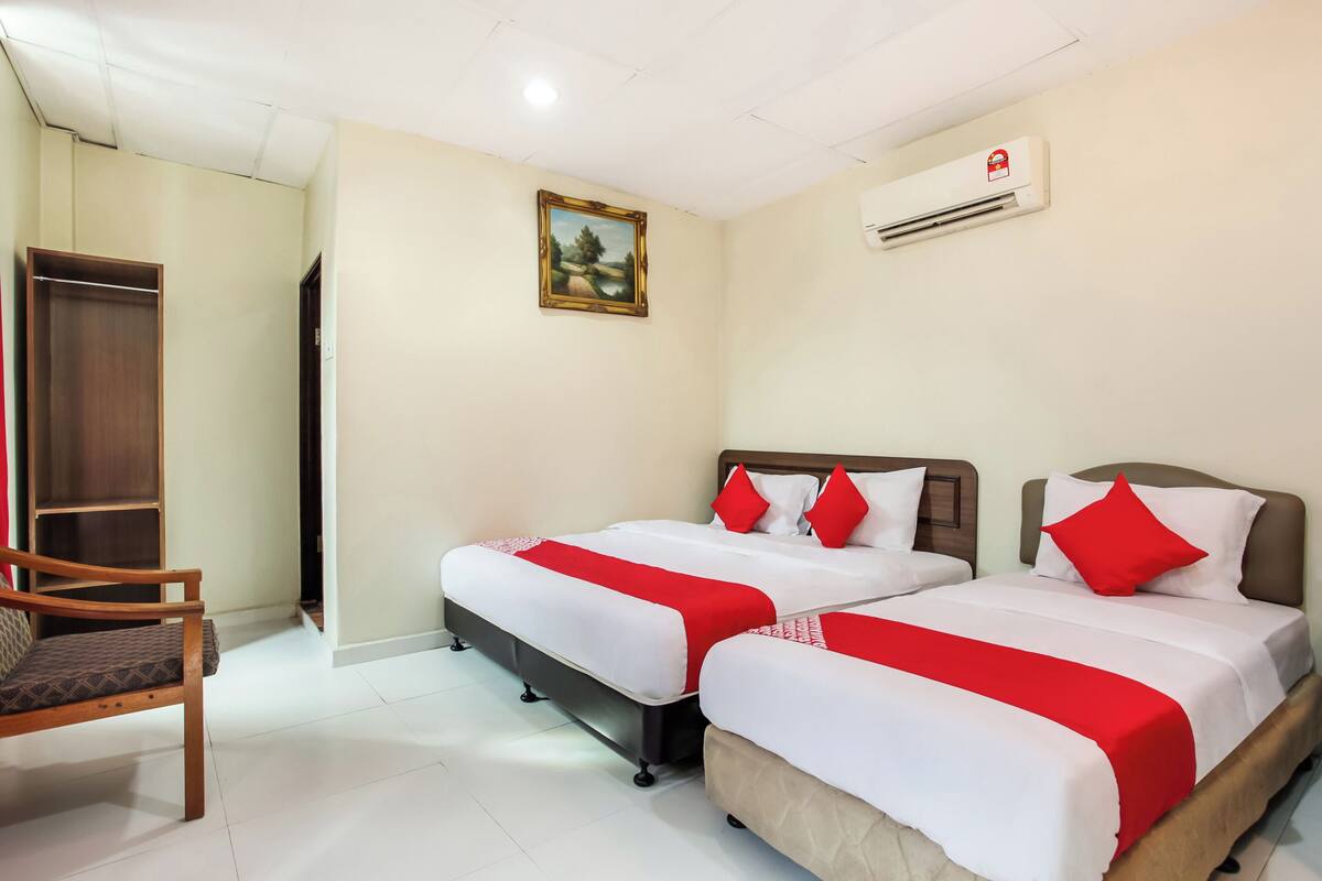 Een hotelkamer met twee bedden, een houten stoel, een garderobe, een schilderij en een airconditioner.