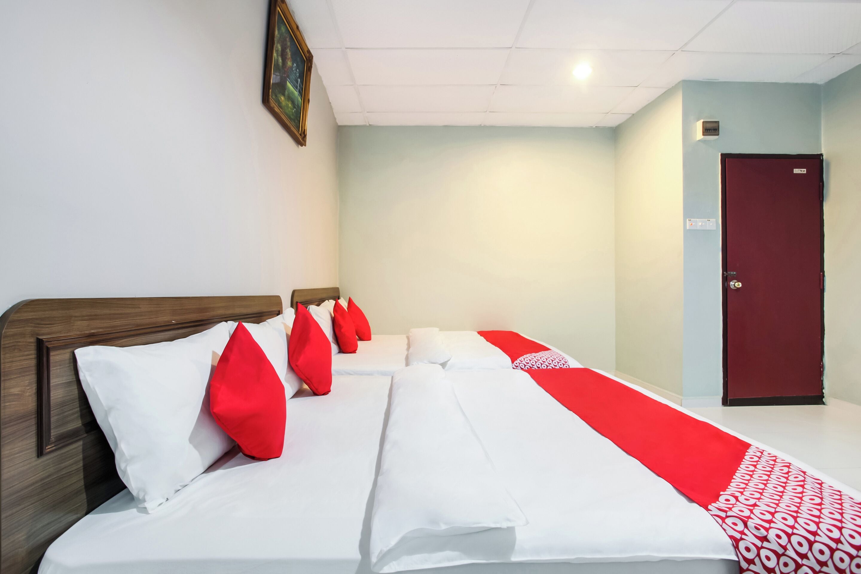 A hotel room with a large bed, a red door, and a white ceiling.
