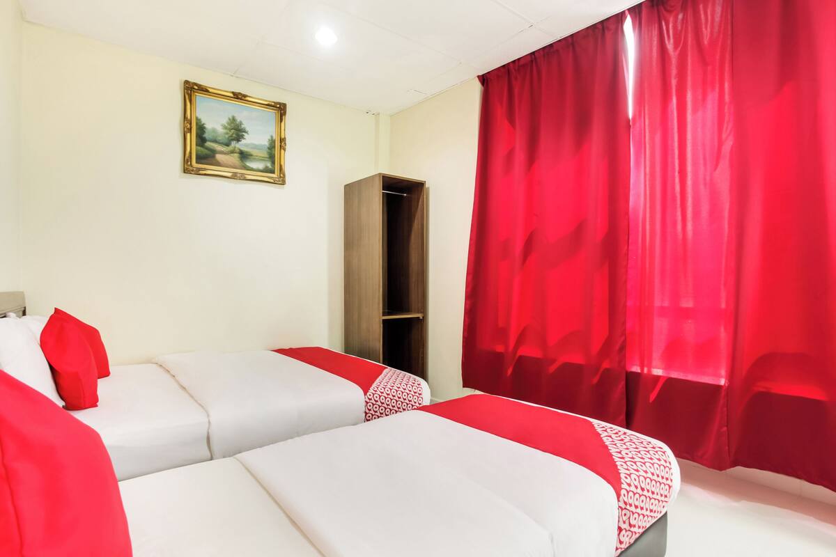 Een hotelkamer met twee bedden, een kledingkast, een schilderij aan de muur en rode gordijnen.