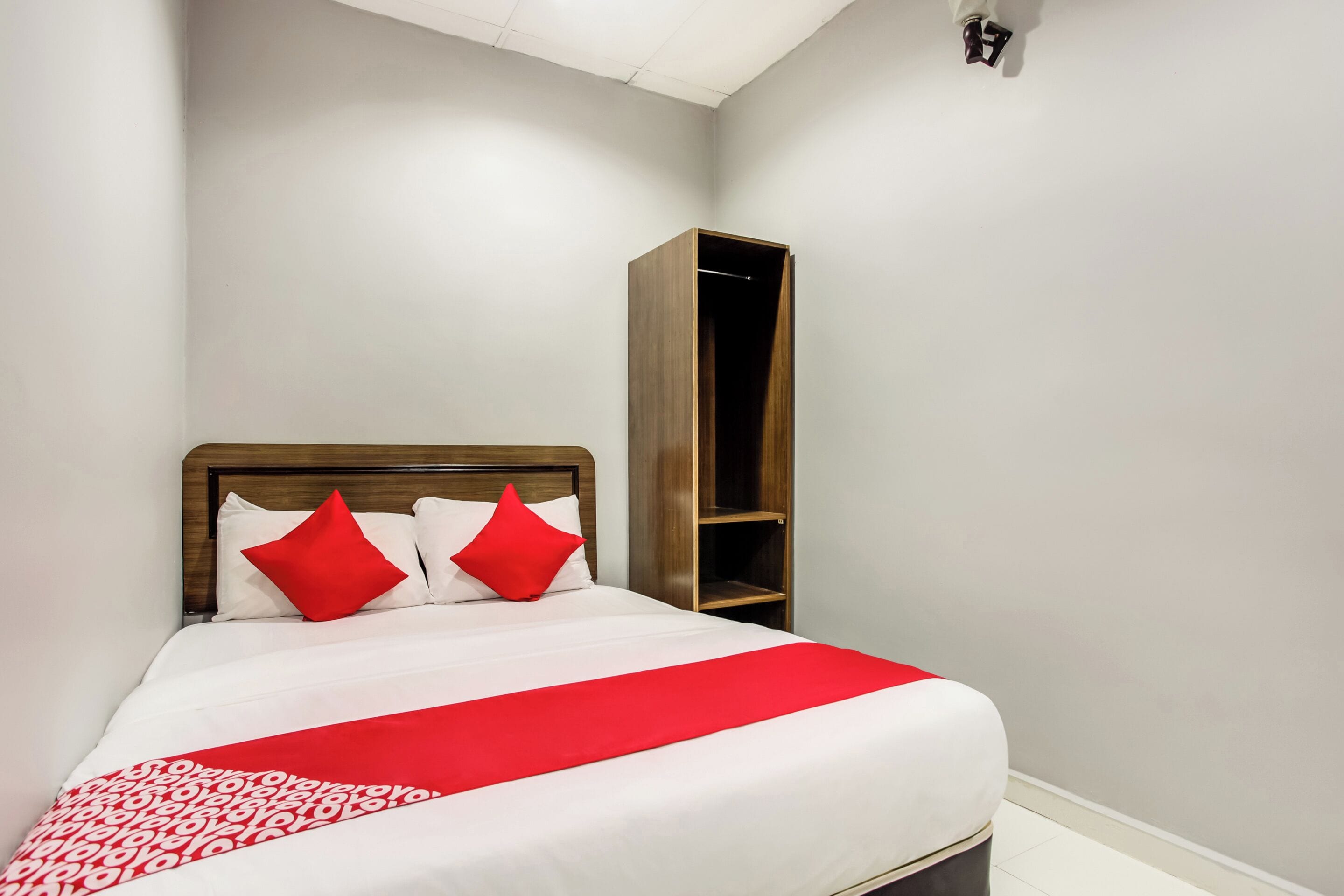 A neatly made bed with a red and white bedspread, two red pillows, and a wooden headboard.