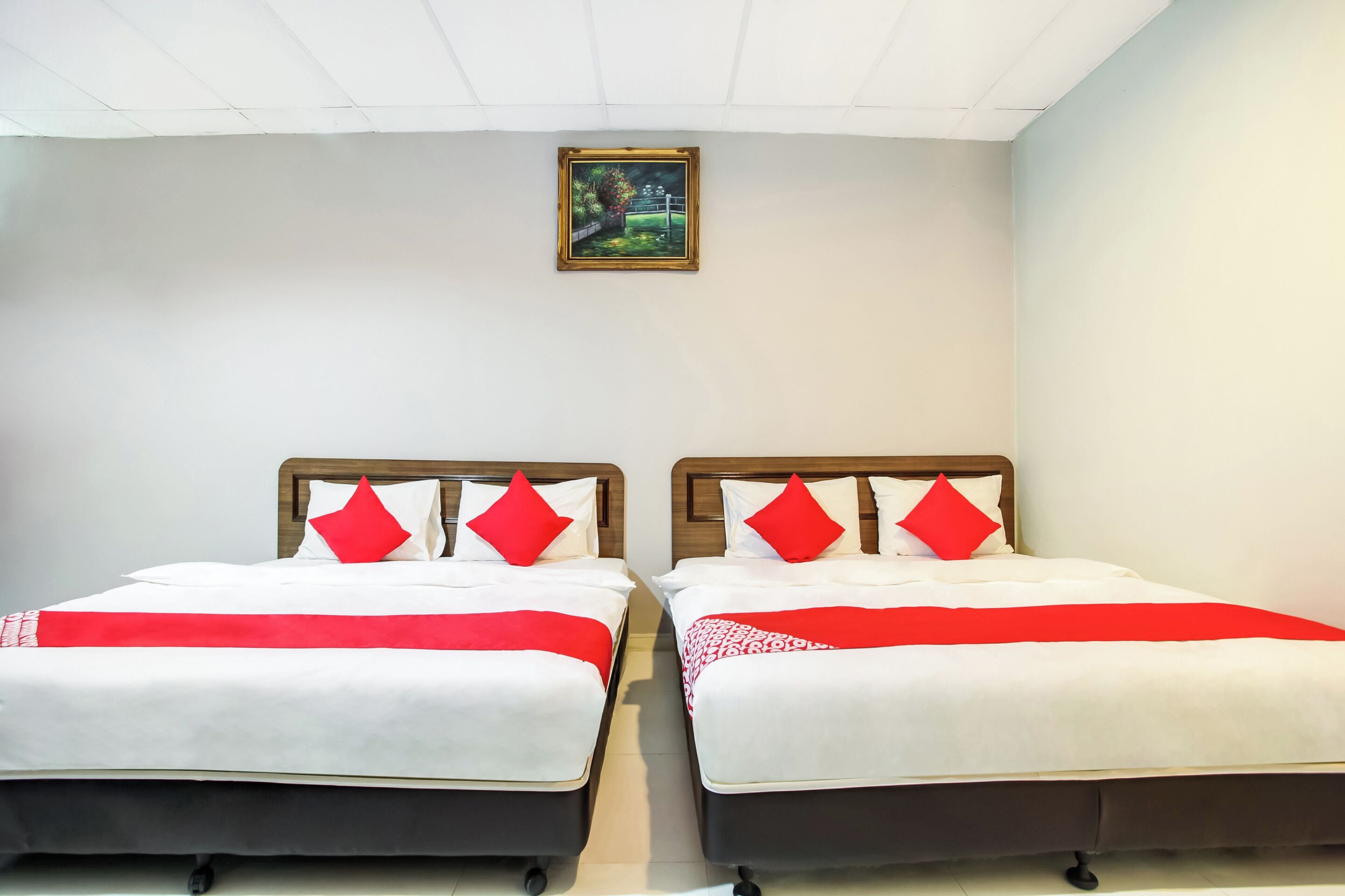 Due letti con biancheria da letto bianca e rossa, una coperta rossa e un quadro appeso al muro.