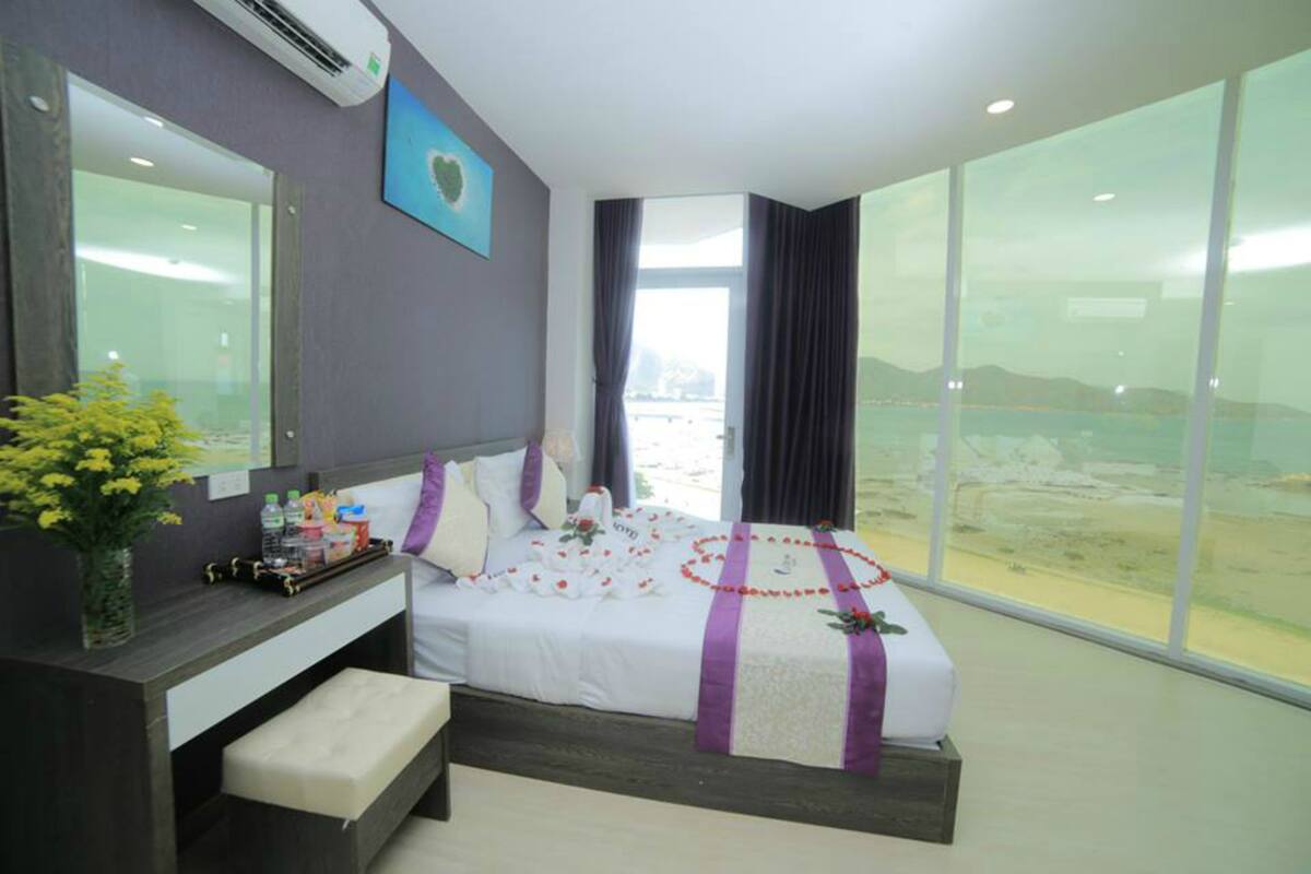 A hotel room with a large bed, a bedside table with a vase of flowers, a view of the desert through large windows, and a modern design.