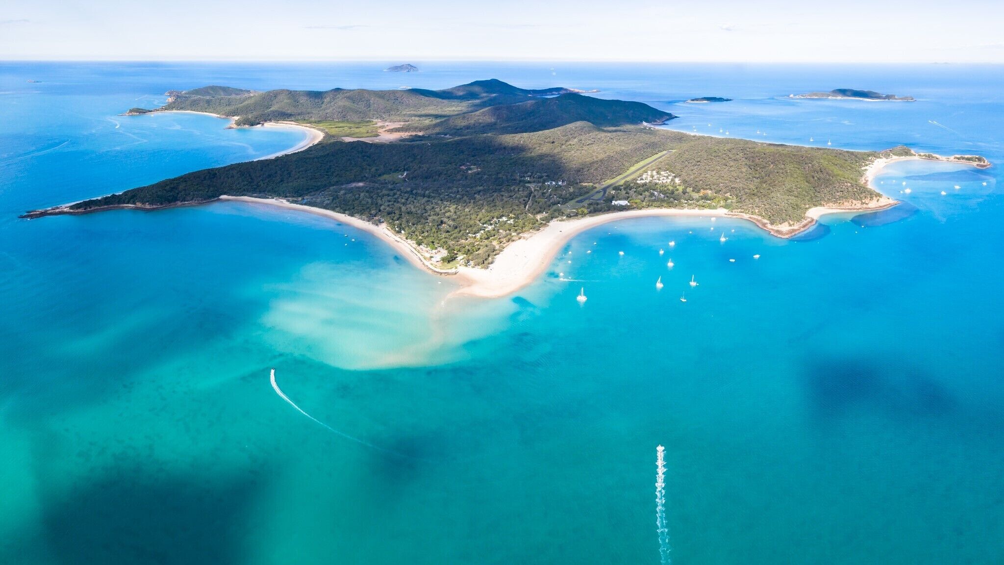 An aerial view of a coastal island with clear blue waters, sandy beaches, and lush greenery.