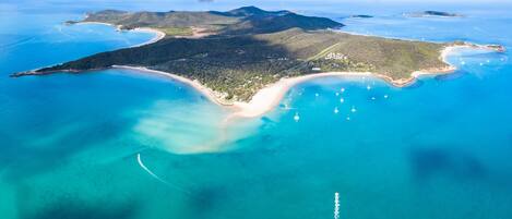 An aerial view of a coastal island with clear blue waters, sandy beaches, and lush greenery.