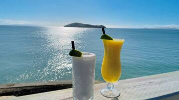 Dos bebidas sobre una terraza de madera con vista al océano y una isla distante.