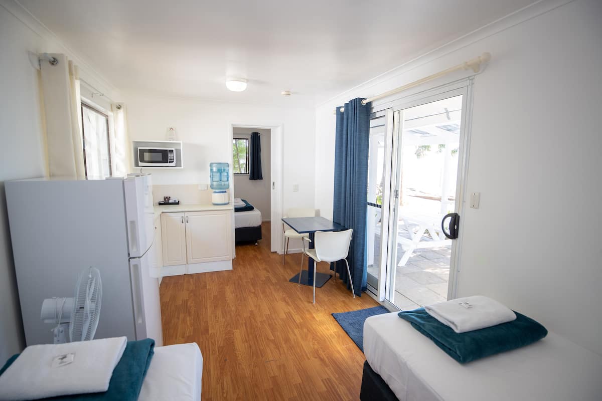 Habitación de hotel compacta con kitchenette, zona de comedor y cama con manta azul.