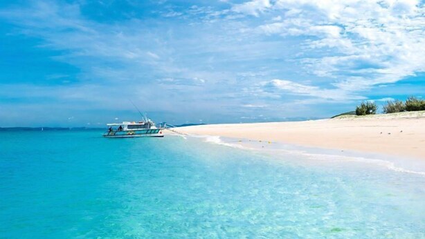 Una playa con agua turquesa cristalina y un barco fondeado en la orilla.