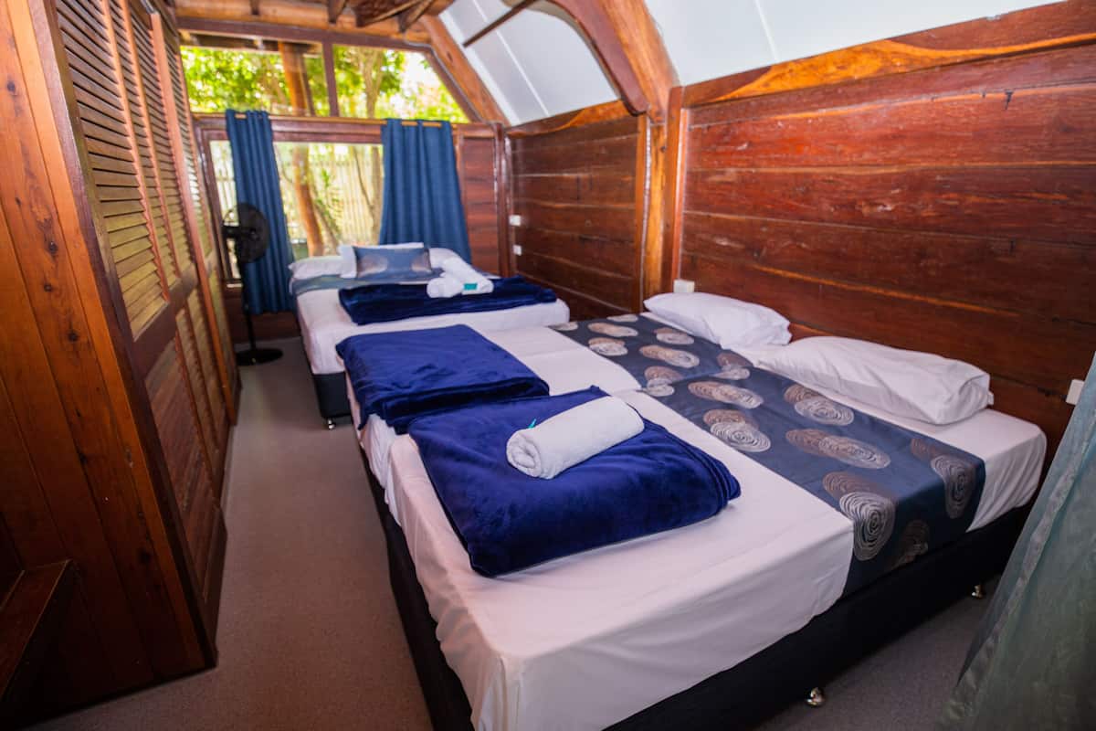 Una cabaña con tres camas de madera, cada una con una manta azul y sábanas blancas.