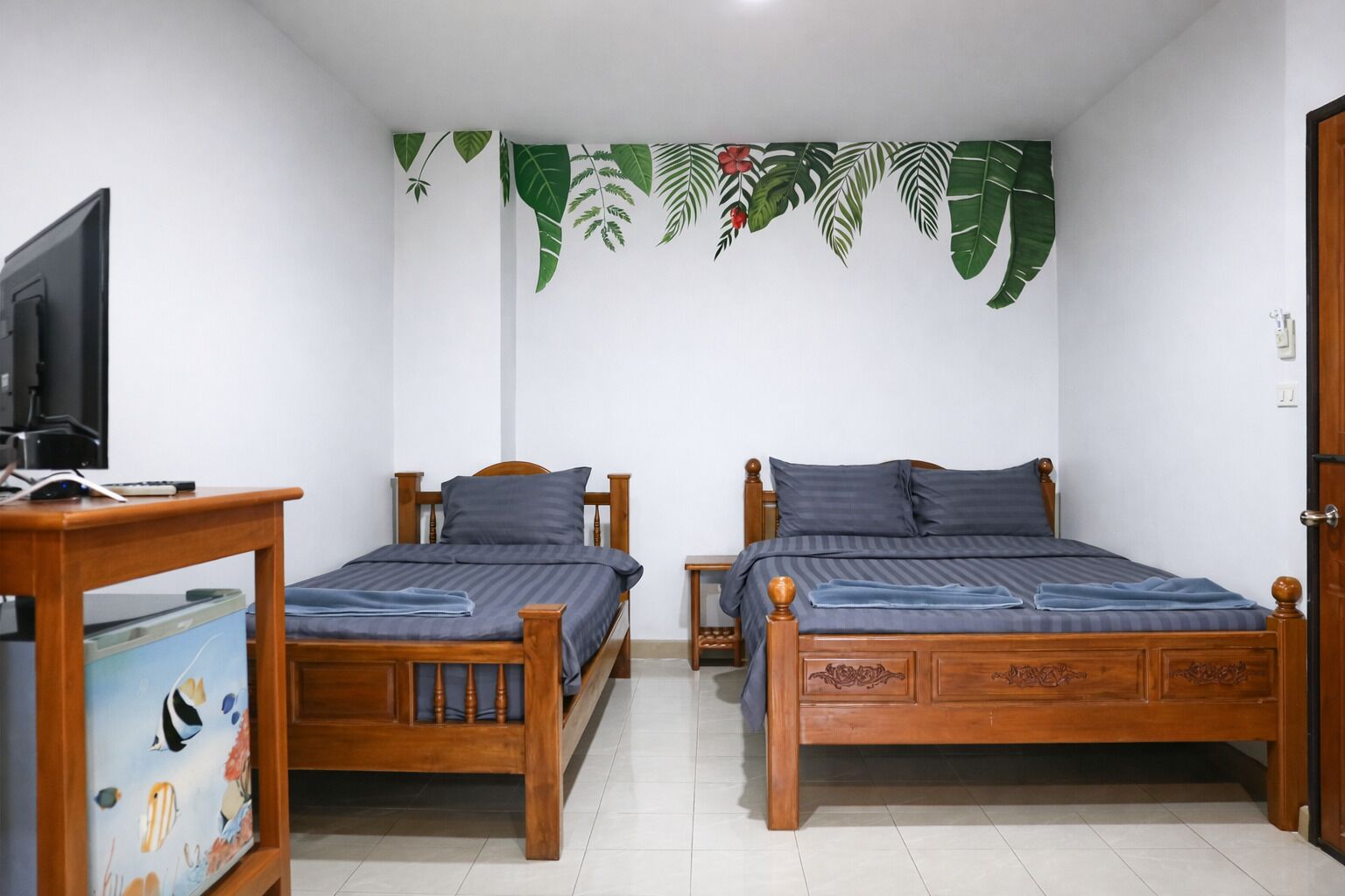 Una habitación con dos camas de madera, un televisor a la izquierda y un muro decorado con motivos de hojas.