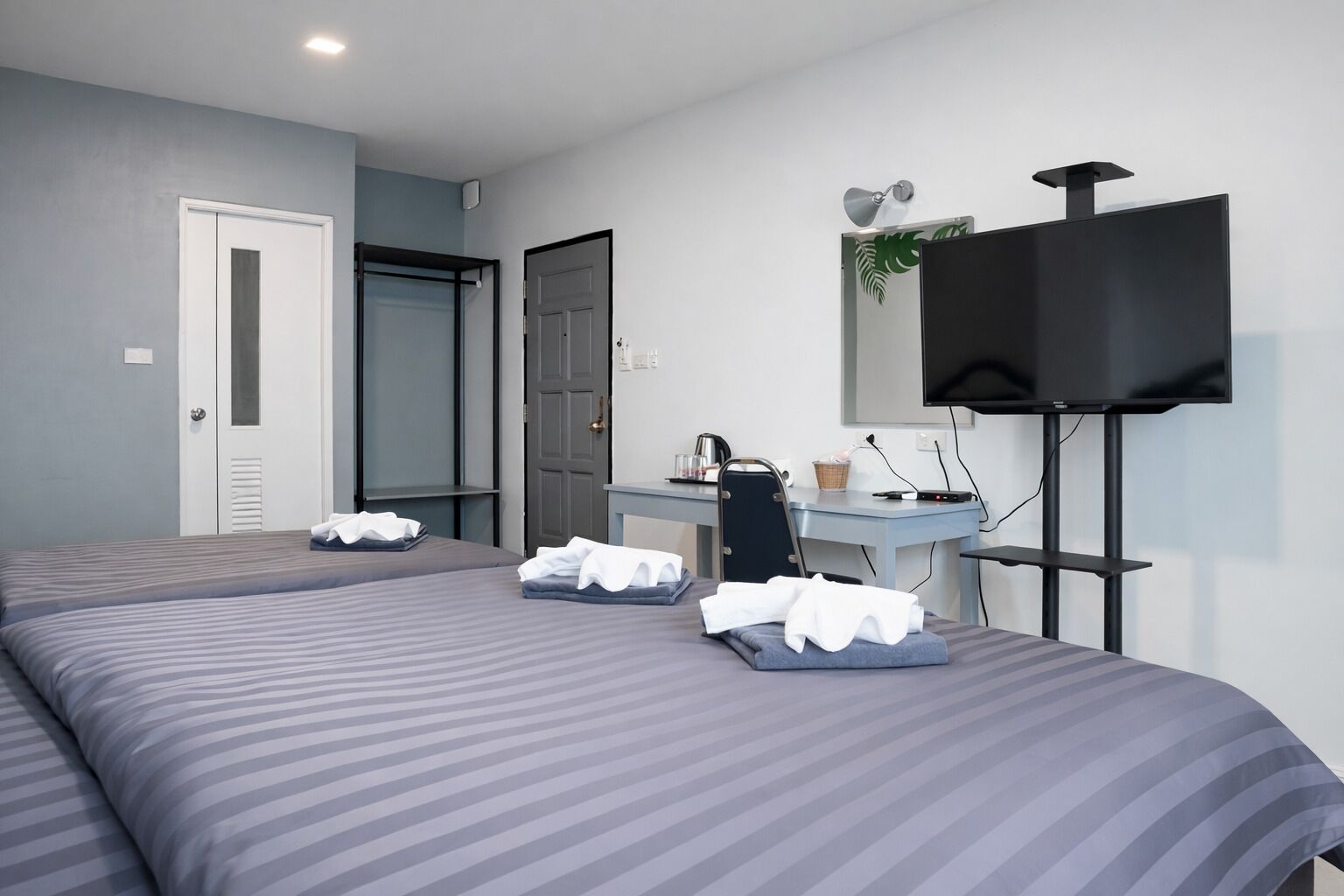 A hotel room with two beds, a desk, a chair, a television, and a door.